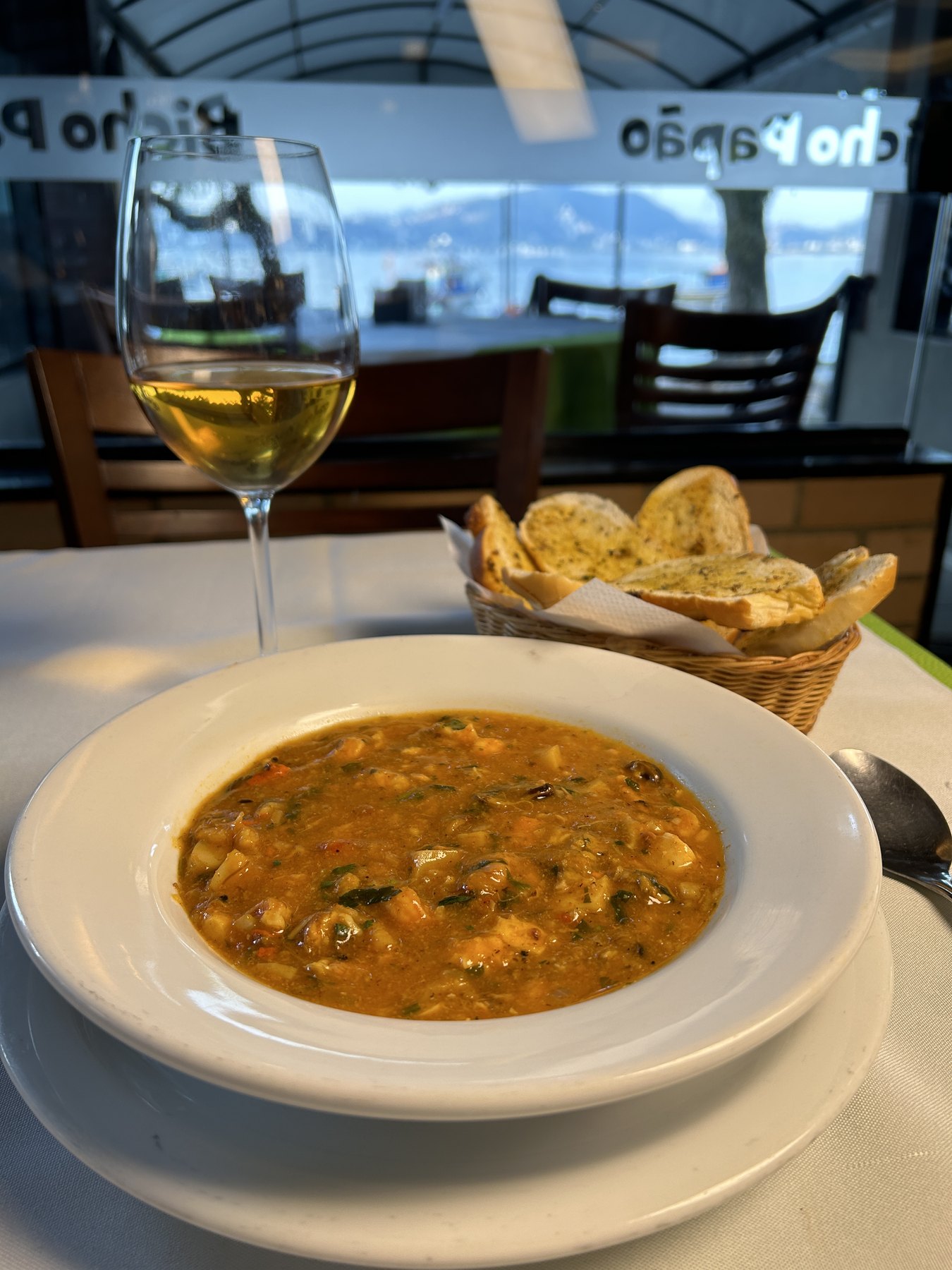 Prato fundo com sopa Leão Veloso servida com cesta de torradas de alho e taça de vinho branco, com a Baía de Guanabara ao fundo